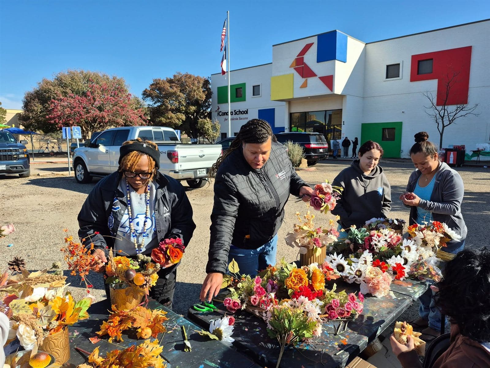 Four neighbors arranging fall flowers at a table in front of the Condra School