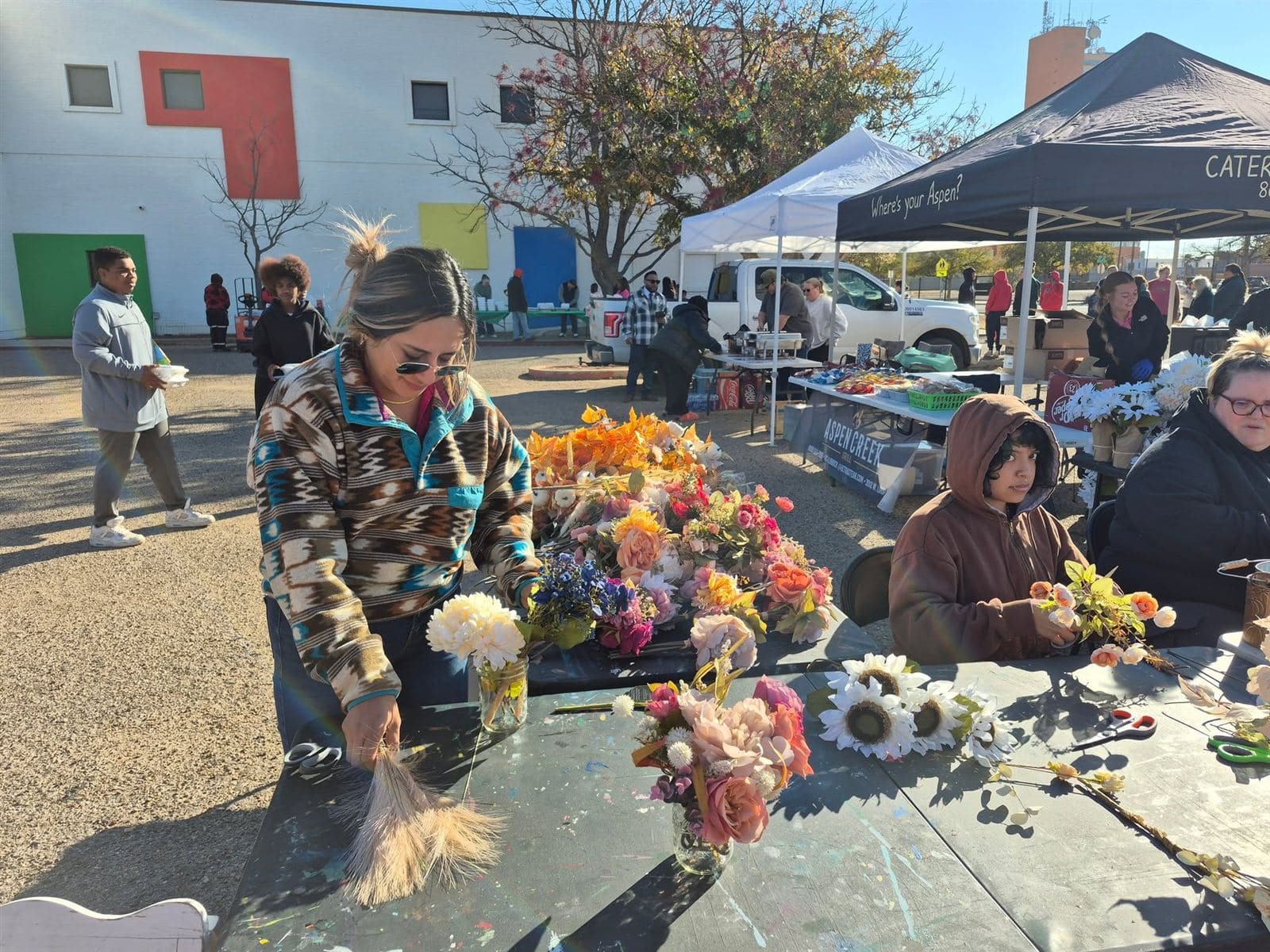 A busy flower table with a neighbor arranging stems
