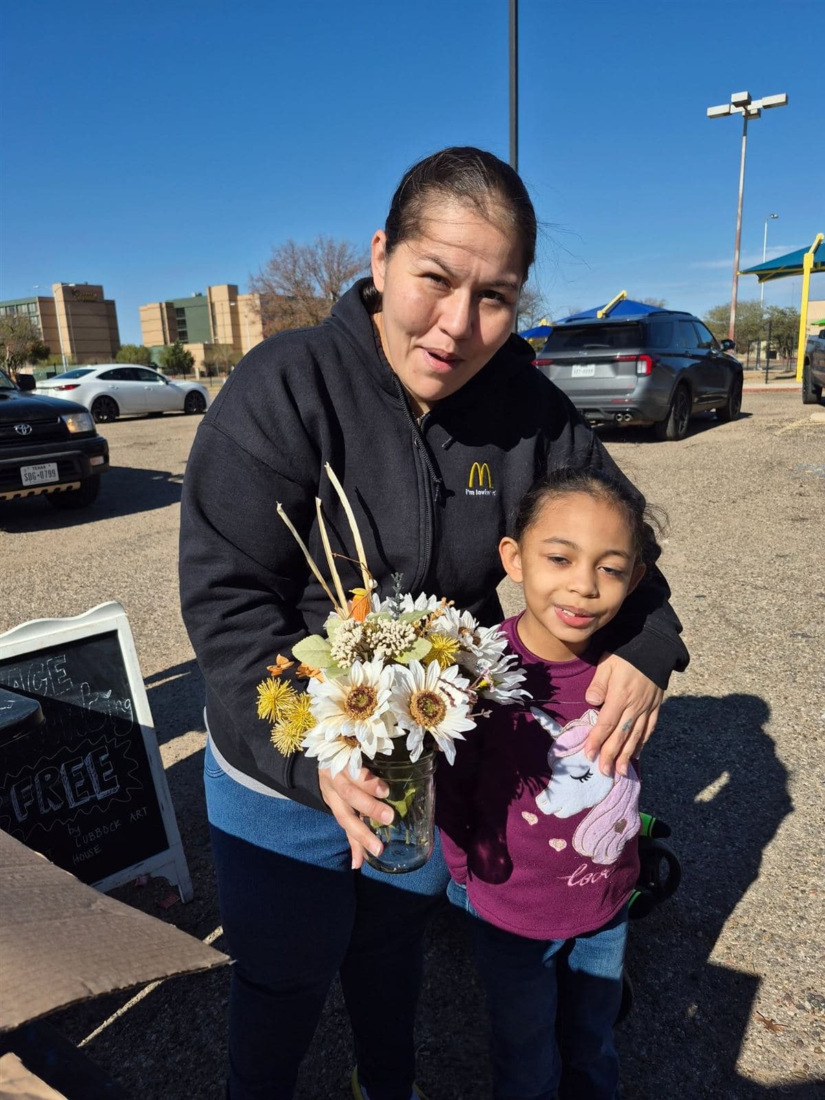 A mother and young daughter with a bouquet beside a chalkboard sign that says free