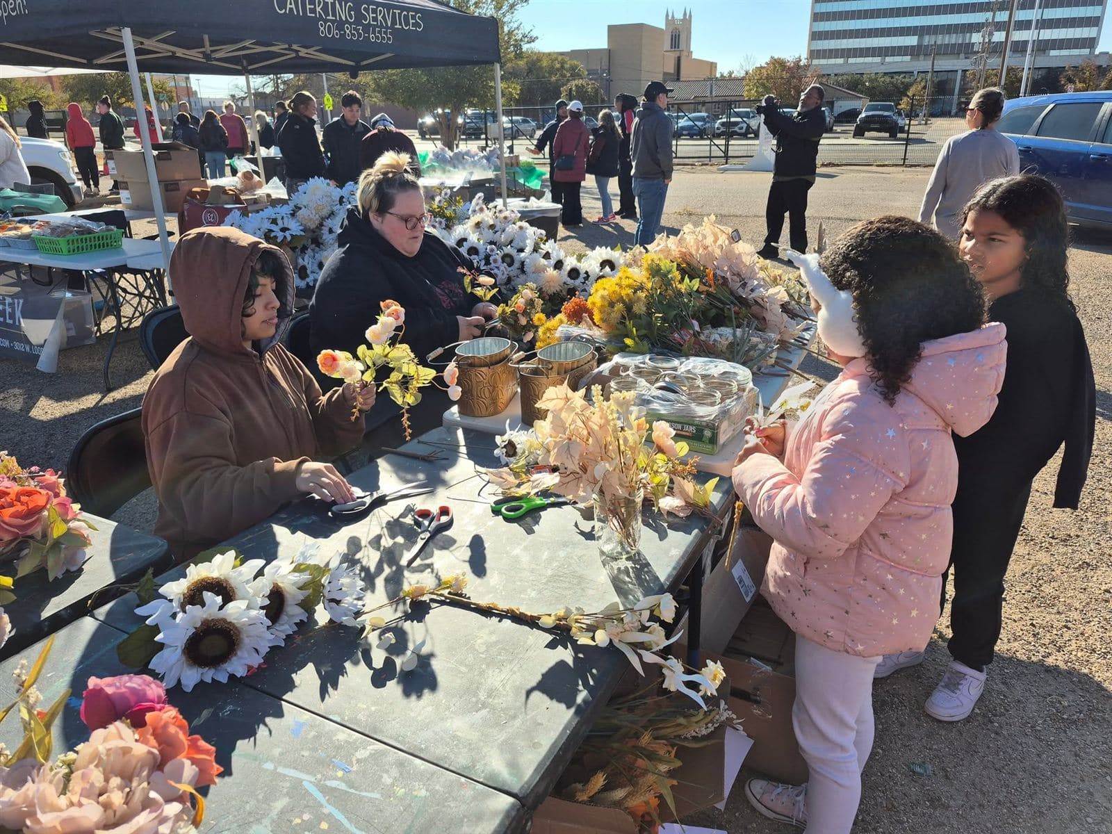 A wide view of the flower table with a seated volunteer and kids