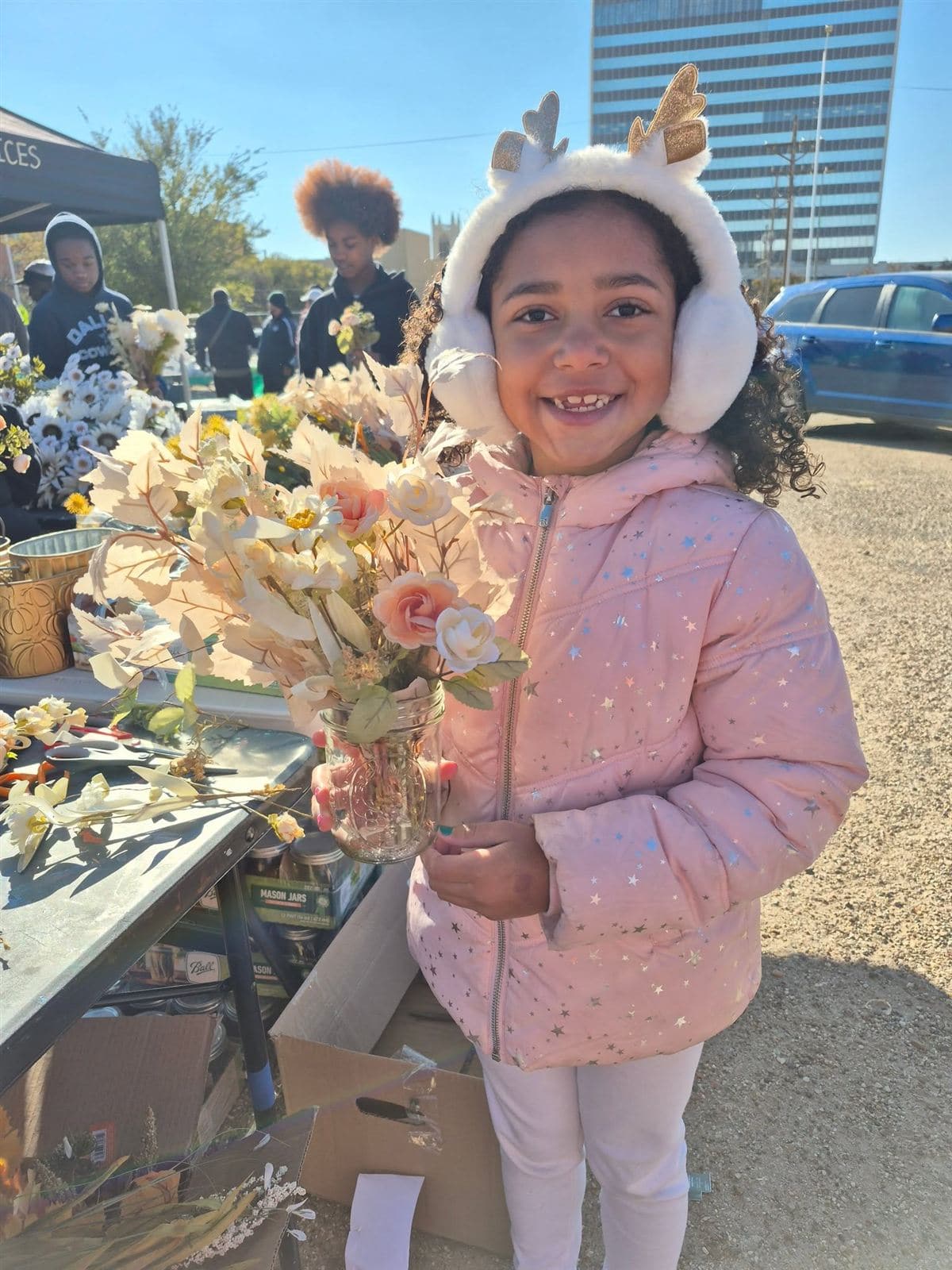 A young girl in reindeer earmuffs smiling with her jar bouquet