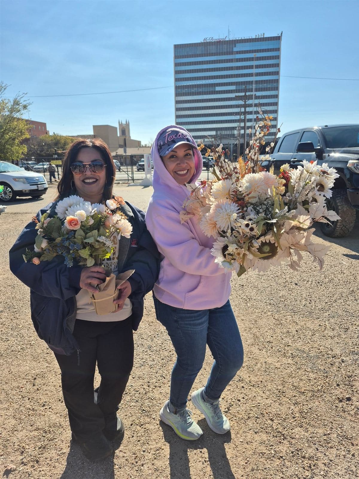 Two neighbors holding large bouquets with downtown Lubbock behind them