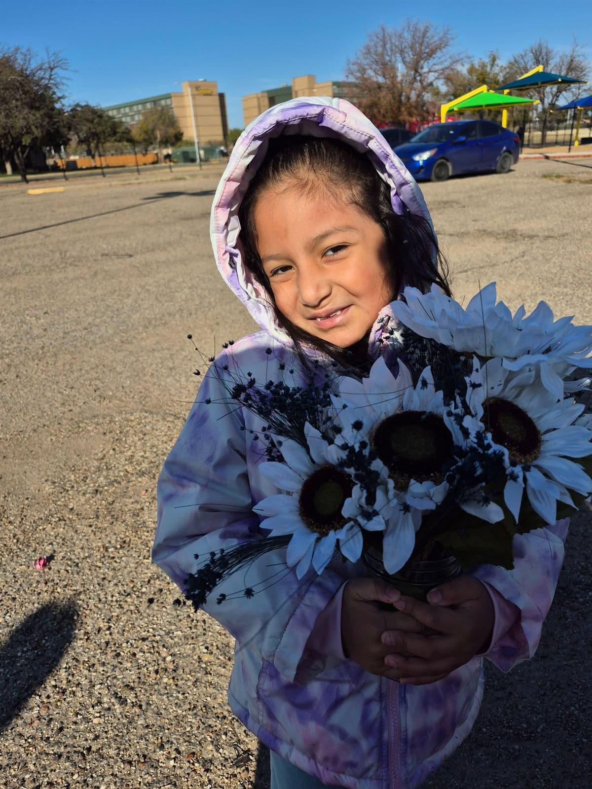 A little girl in a purple hood holding a sunflower bouquet